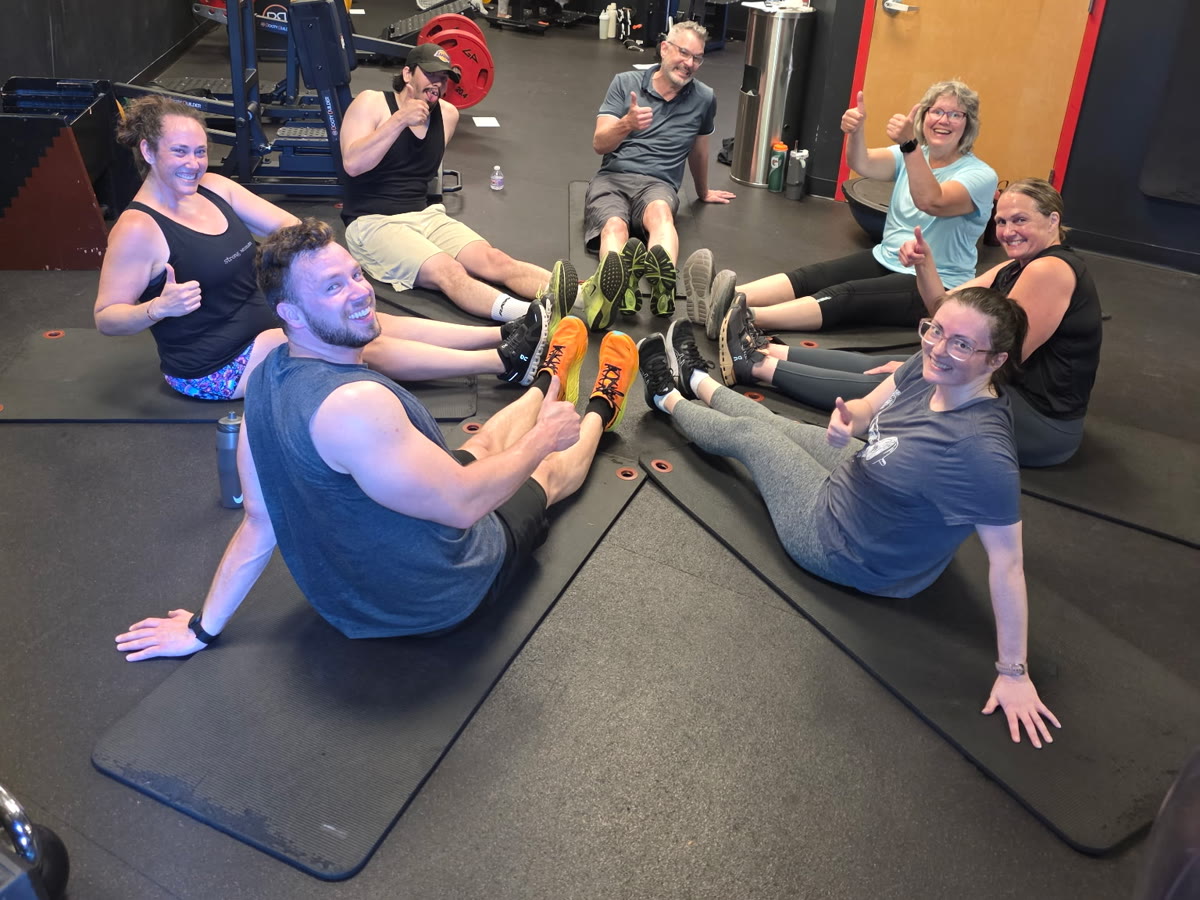 Seven members giving a thumbs up in a circle on the mats after a small group training class